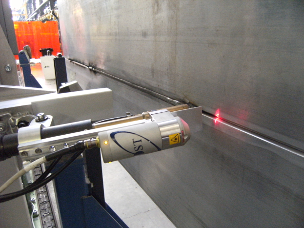 Eine Laserschneidmaschine in einer Fabrik, die helles Licht ausstrahlt, mit einer Wand auf der rechten Seite und Gegenst"anden im Hintergrund.