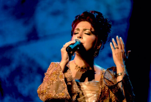 Eine Frau in einem goldenen Kleid singt auf der Bühne der Eurovision in ein Mikrofon mit einem blauen und schwarzen Hintergrund.