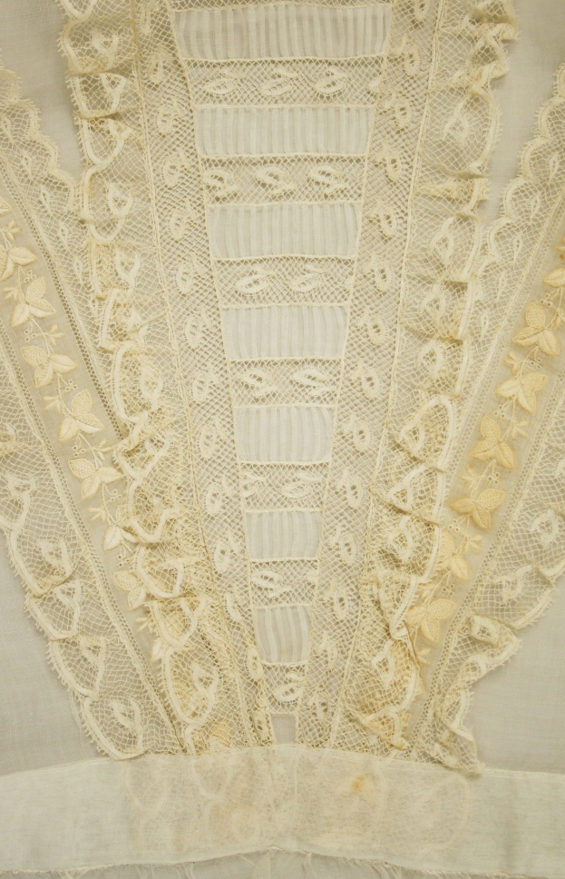Nahaufnahme eines weißen Kleides mit zarter, detailreicher Spitzenverzierung mit verschiedenen Mustern auf einem leichten, luftigen Stoff.