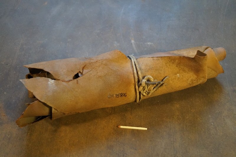 Papiertüte in Form einer Granate mit Henkel, enthaltend eine Zigarette, auf einem Tisch neben einer unangezündeten Zigarette.