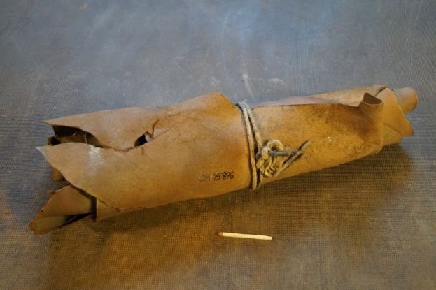 Papiertüte in Form einer Granate mit Henkel, enthaltend eine Zigarette, auf einem Tisch neben einer unangezündeten Zigarette.