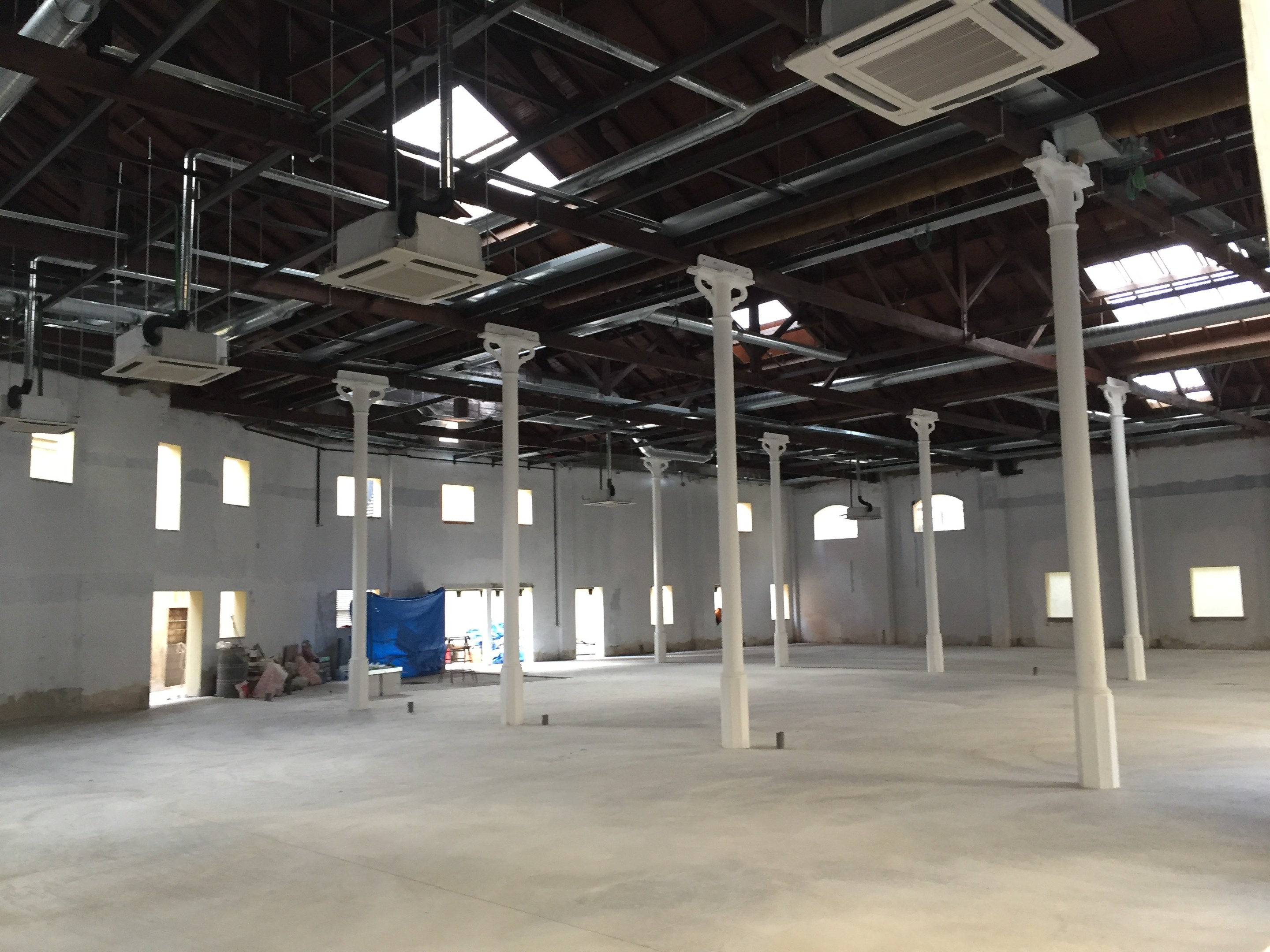 Großer Industriehallenraum mit zahlreichen Fenstern, Säulen und Deckenbeleuchtung, mit hoher Decke mit Klimaanlagen und Betonboden.