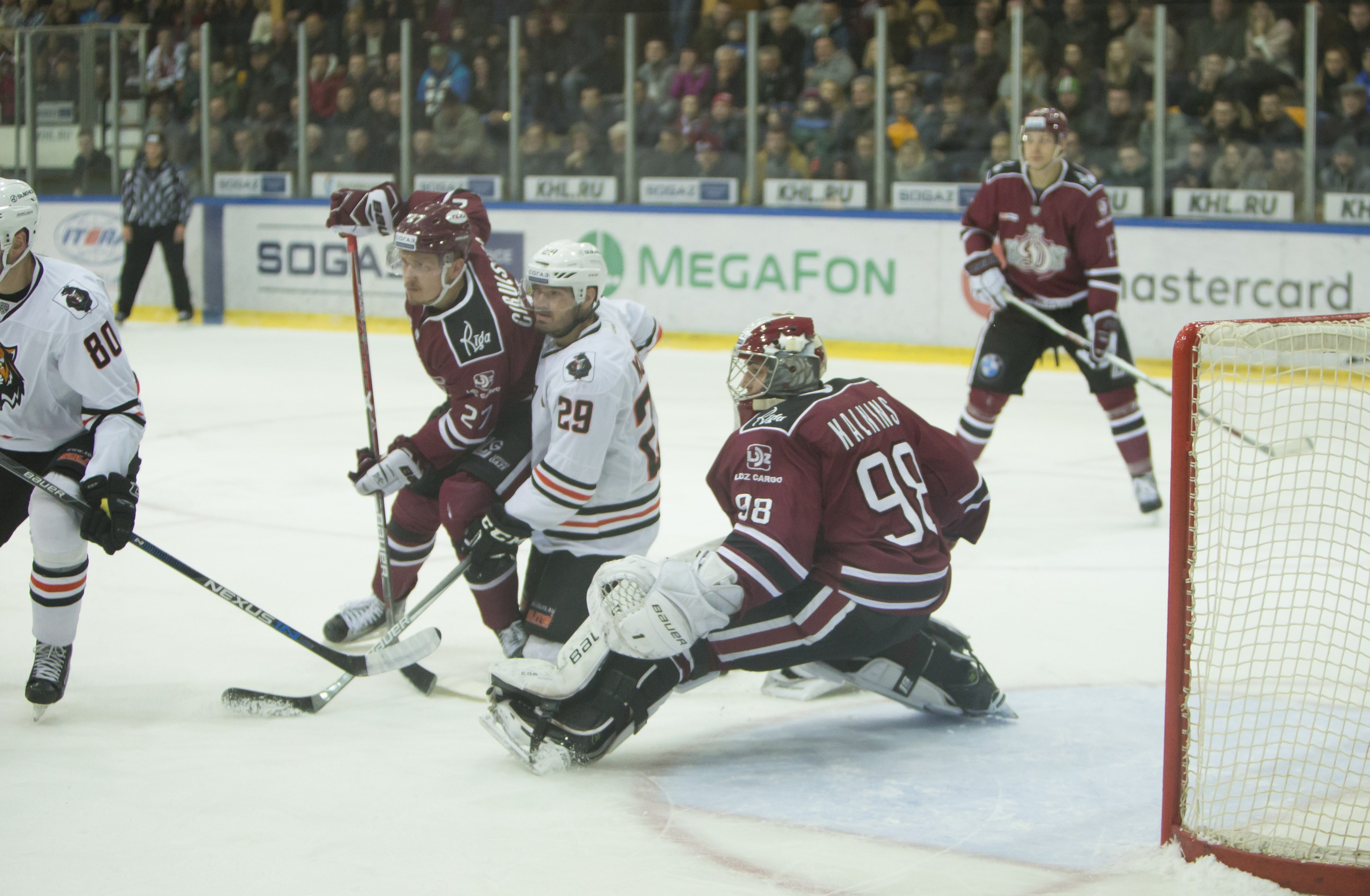 Gruppe von Menschen in Helmen und Hockey-Ausrüstung auf einem Eisstadion mit einem Tor auf der rechten Seite, Zuschauern in den Rängen und Bannern im Hintergrund.