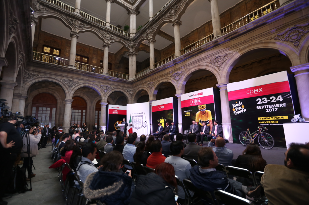 Eine Gruppe von Menschen sitzt an einem Tisch mit einem Podium und einem Mikrofon vor einer Menge, Kameras und Bannern, was auf eine Pressekonferenz f├╝r das CDMX 2017-Event hindeutet.