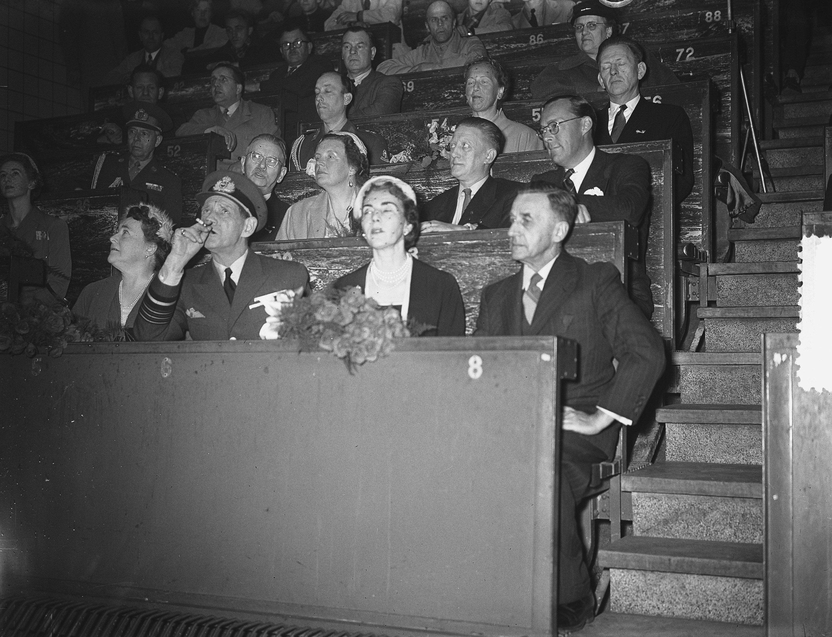 Schwarzes und weißes Foto einer Zuschauermenge in einem Stadion, die einer Tribüne mit einem Blumenstrauß gegenüberstehen, Treppen auf der rechten Seite sichtbar