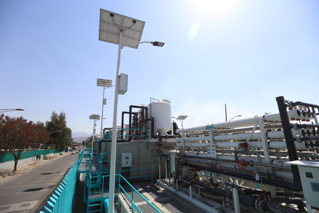 Großes industrielles Gebäude mit ausgedehnten Rohrleitungen, Solarpanelen, Geländern und Infrastruktur, vor einem Hügel und einem klaren Himmel, Teil einer Wasseraufbereitungsanlage in Kalifornien.