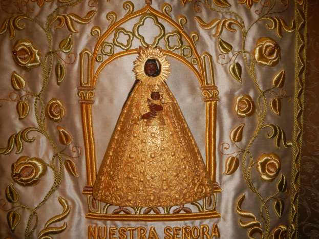 Goldbrokat-Chorrock mit einer friedlichen Frau in einem hochgeschlossenen, langärmeligen Kleid mit einem Dutt, umgeben von kunstvollen Texten und Designs in einem goldenen Rand.