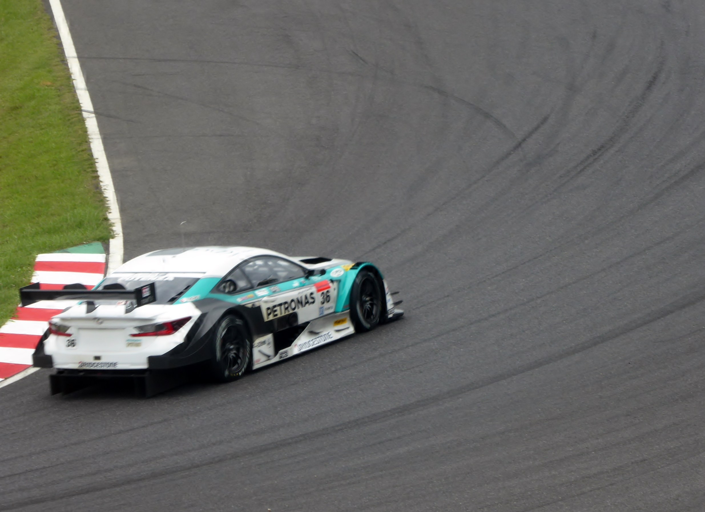 Ein Mercedes-AMG GT3 Rennwagen auf einer Rennstrecke mit Text auf seiner Karosserie und Gras links.