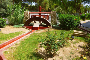 Minigolfanlage im Park mit Grünflächen, einer Straße mit Fußgängern, Hinweisschildern und einem klaren Himmel im Hintergrund.