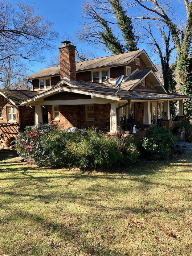 Ein Haus mit einem durch einen Sturm beschädigten Dach umgeben von Pflanzen, Gras, Bäumen und unter einem bewölkten Himmel.