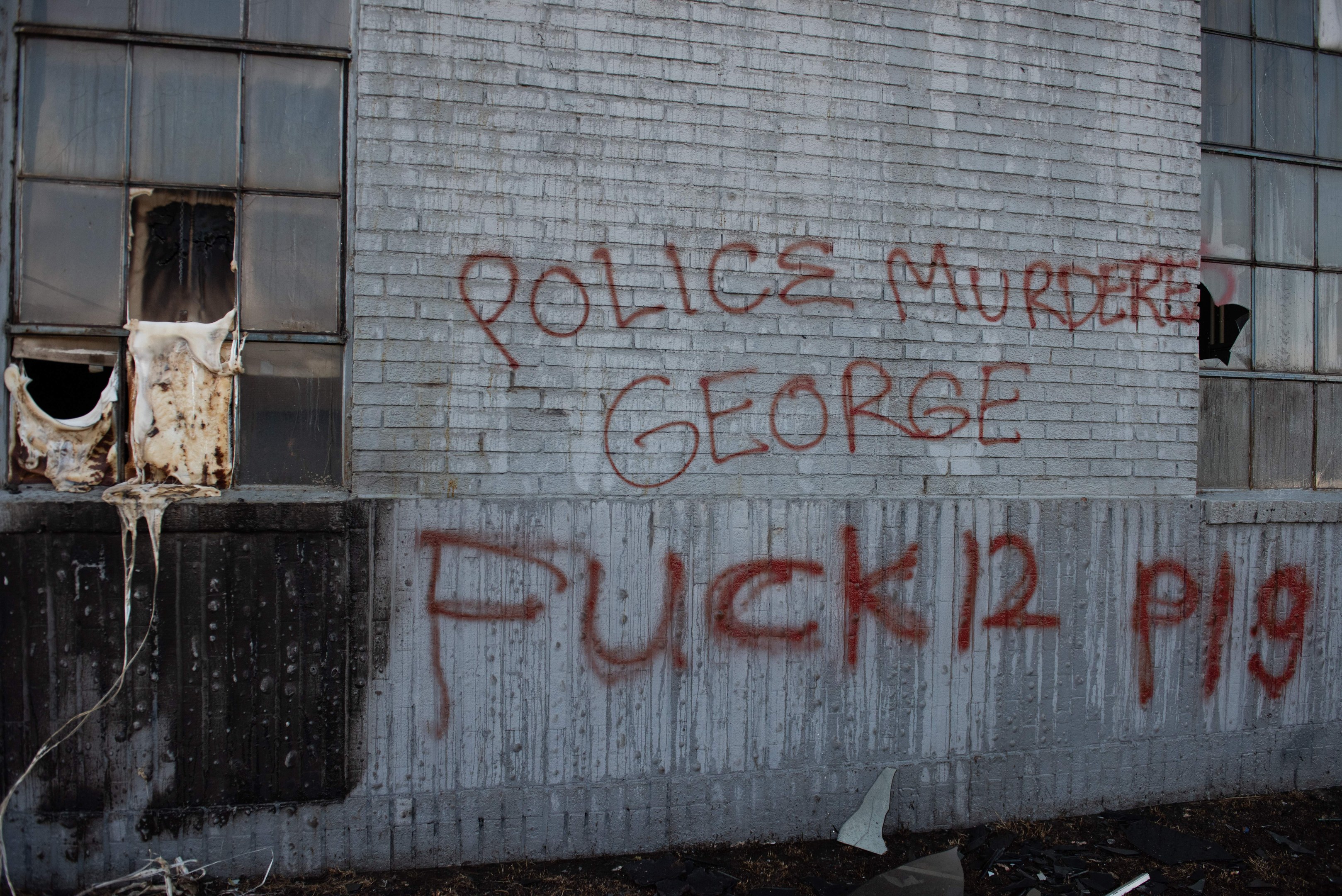 Graffiti an einer Hauswand mit der Aufschrift "Polizeimord George Fuck 12 P19" mit Fenstern und verstreuten Gegenständen davor.